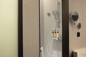 Et moderne badeværelse med brusekabine i glas, spejl på væggen og en hylde med toiletartikler.