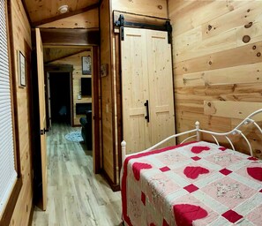Een smalle houten gang die leidt naar een slaapkamer met een bed en een deur.