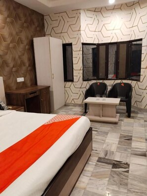 A hotel room with a bed, a desk, a chair, a mirror, and a window. - Hotel Aurum Mansarovar (Jaipur)