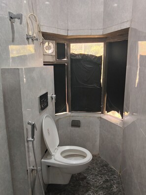 A bathroom with a toilet, shower, and a window with a black covering. - Hotel Aurum Mansarovar (Jaipur)