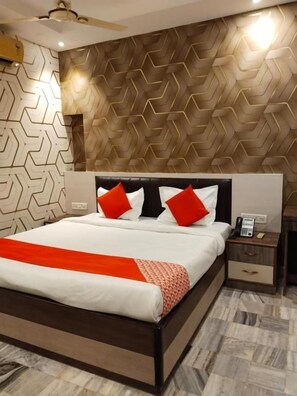 A modern bedroom with a large bed, a nightstand with a phone, and a patterned wall. - Hotel Aurum Mansarovar (Jaipur)