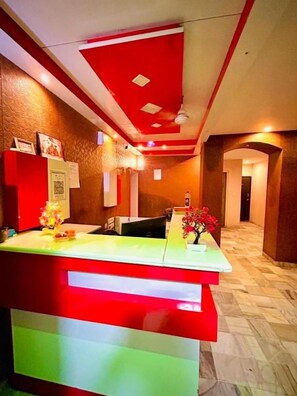 A reception area with a counter, framed pictures, and a vase with flowers. - Hotel Aurum Mansarovar (Jaipur)
