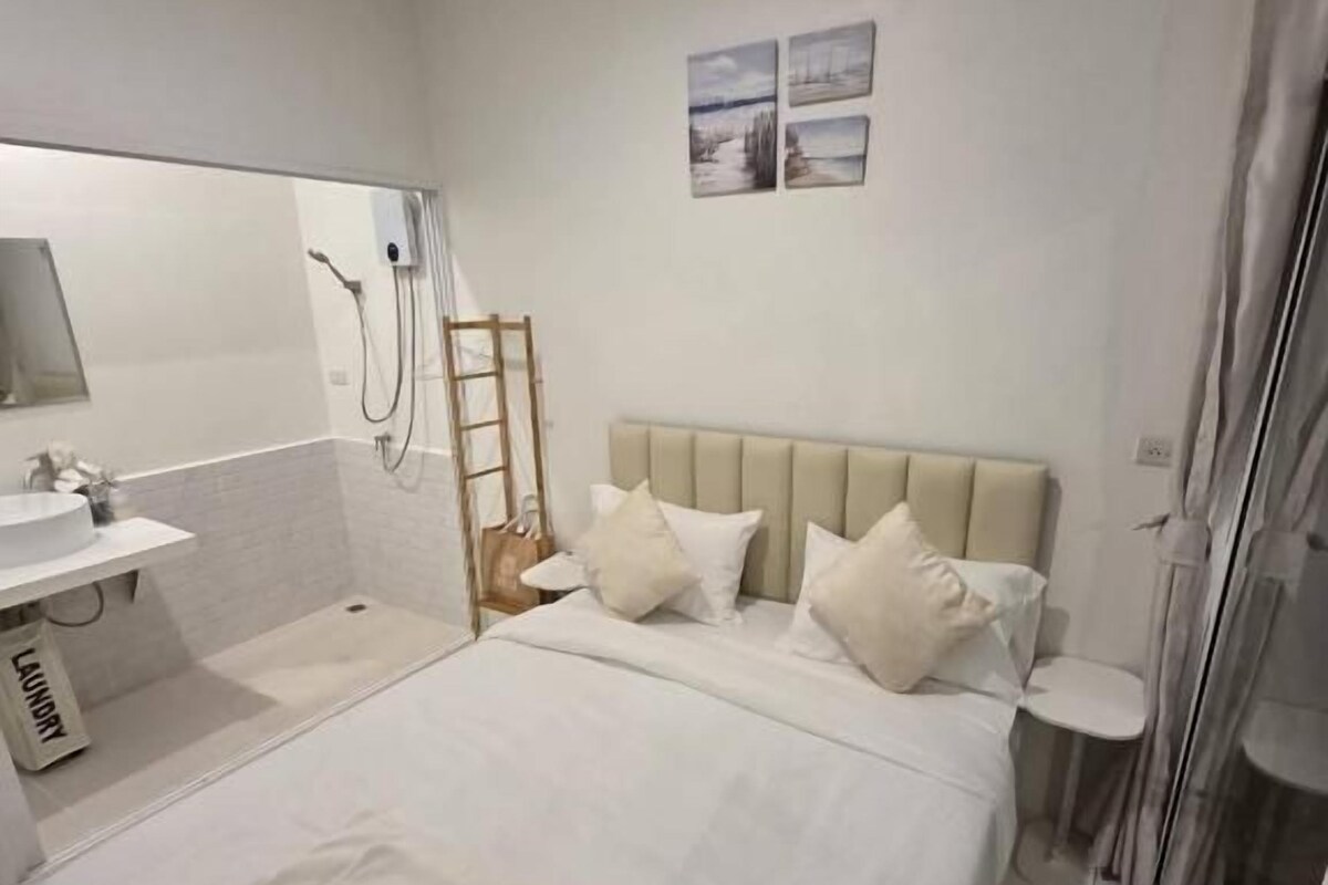A hotel room with a bed, a bedside table, a mirror, and a shower area.