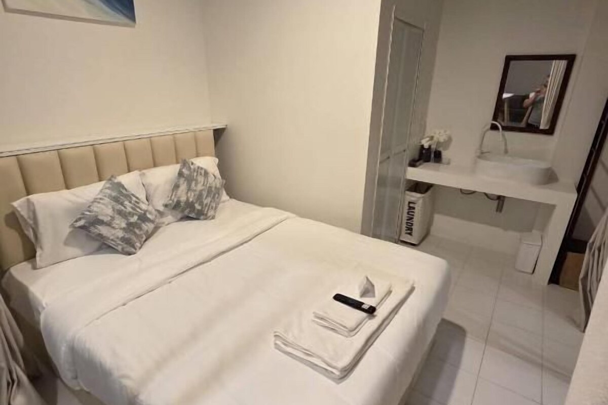 A hotel room with a bed, a bedside table, a mirror, and a bathroom area.