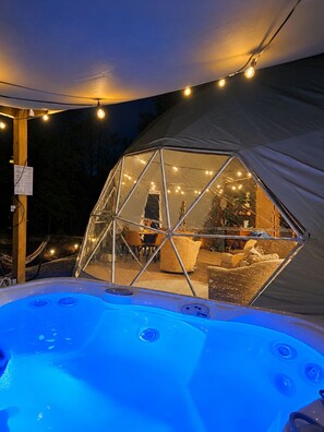 Une tente en forme de dôme avec un jacuzzi à l’avant, des guirlandes lumineuses et une vue sur l’intérieur.