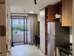Eine kompakte Küche mit Kühlschrank, Herd und Holzausstattung. Eine Glasschiebetür führt zu einem Balkon mit Blick auf Gebäude und Grünflächen.
