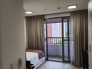 Ein Hotelzimmer mit einem Bett, einem Telefon, einer Fernbedienung und einer Glastür zu einem Balkon.