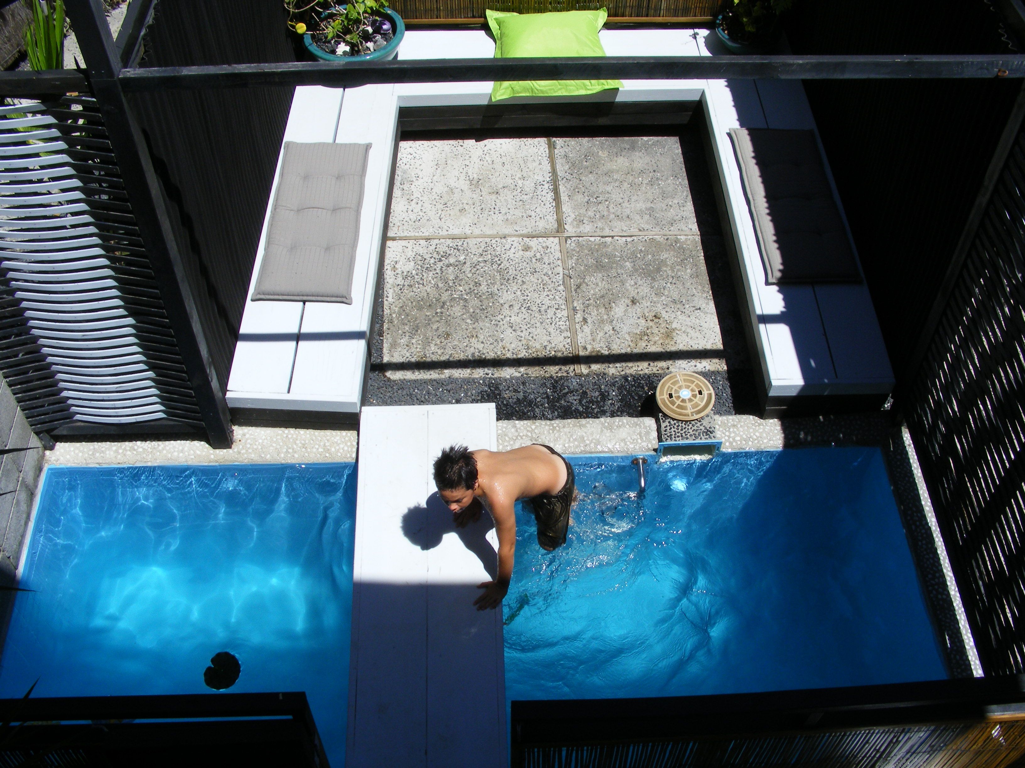 Una piscina con una persona entrando desde una zona de terraza.