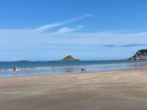 Uma praia com céu claro, faixa de areia e uma colina ao longe.