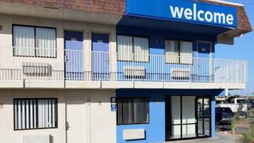 Un motel con un letrero azul que dice 'welcome', habitaciones numeradas y un estacionamiento.