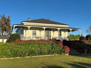 Uma casa de dois andares com varanda, cercada por sebes bem cuidadas e um gramado.