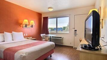 Habitación de hotel con cama, escritorio con televisor, ventana con vistas y lámpara de pared.