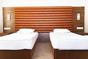 Ett hotellrum med två separata sängar, en sänggavel i trä, vitt sänglinne och ett trägolv.
