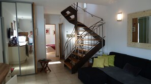 Un salon moderne avec un escalier en colimaçon, un canapé noir et un coin repas doté d’une table en verre.