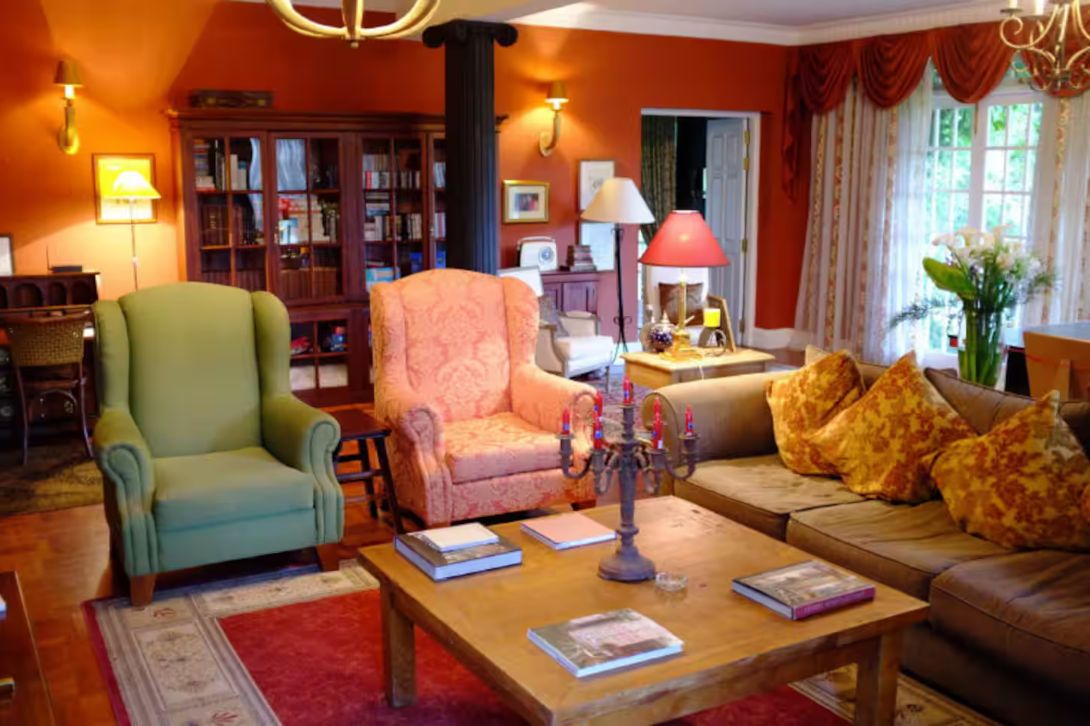 Een gezellige woonkamer met een groene fauteuil, een roze fauteuil, een houten salontafel met boeken, en een bank met decoratieve kussens.