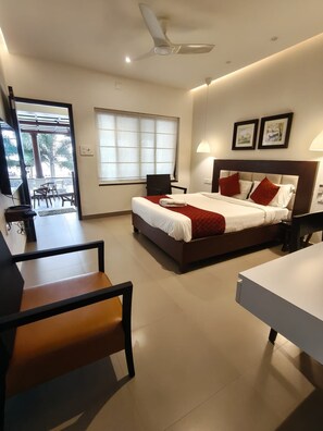 A hotel room with a bed, a desk, a chair, a ceiling fan, and a window with blinds. - Arabian Pearl By Foxin Room (Kochi)