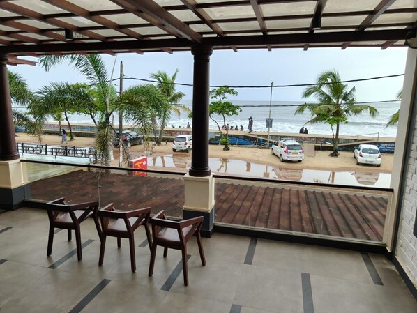 A covered outdoor seating area with a view of the beach and ocean. - Arabian Pearl By Foxin Room (Kochi)