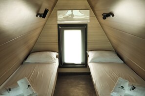 Una piccola stanza triangolare con due letti, una finestra e un lampadario.