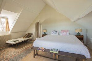 Une chambre avec un grand lit, un banc, une petite table et une fenêtre.
