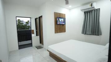 A hotel room with a bed, a television mounted on the wall, an air conditioning unit, and a ceiling fan.