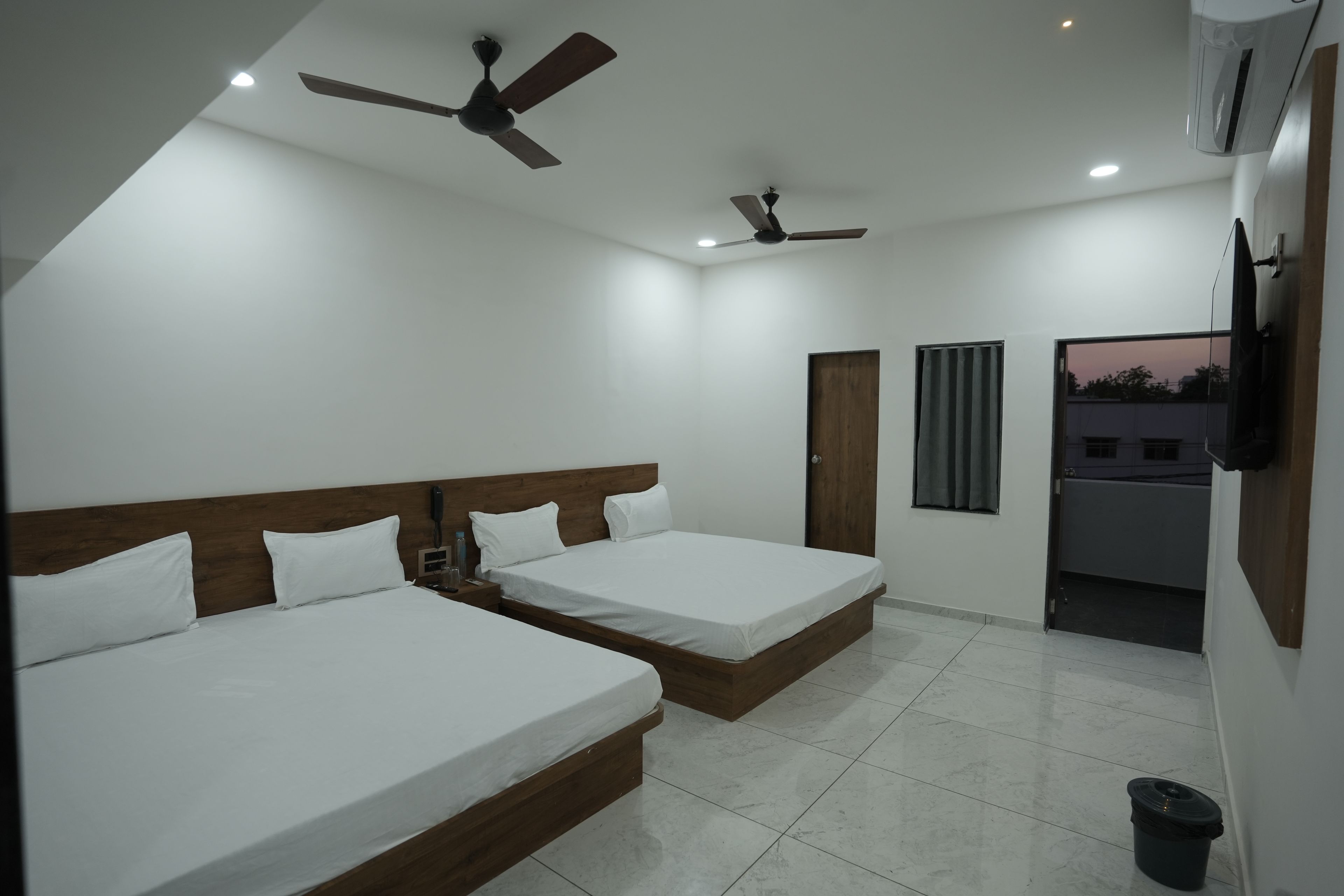 A hotel room with two beds, a ceiling fan, an air conditioning unit, and a view of the outside.