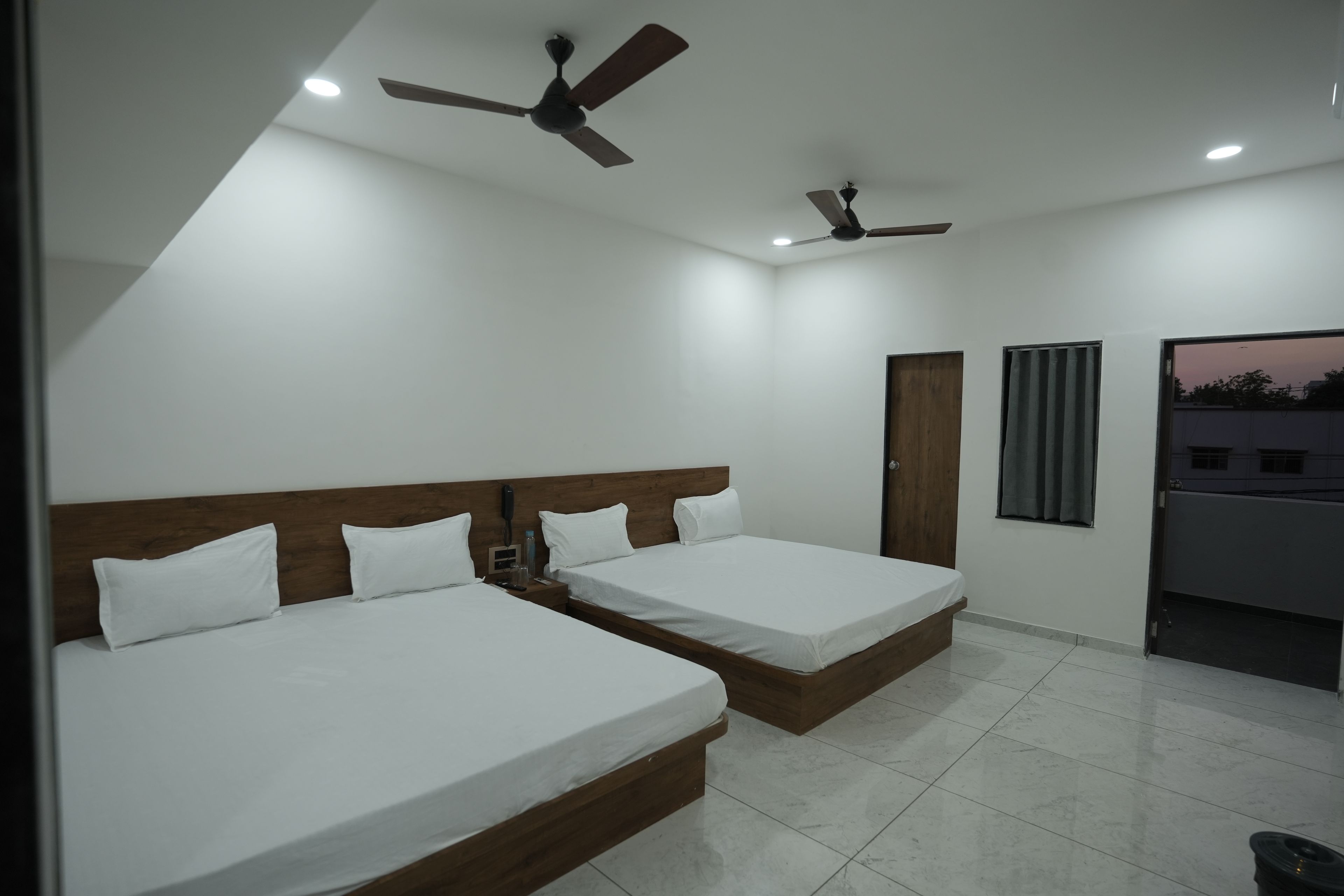 A hotel room with two single beds, a wooden headboard, a ceiling fan, and a window with curtains.