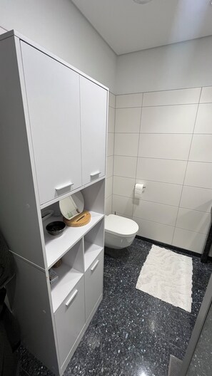 Ein Badezimmer mit Toilette, weißem Schrank, Marmorboden und weißem Teppich.