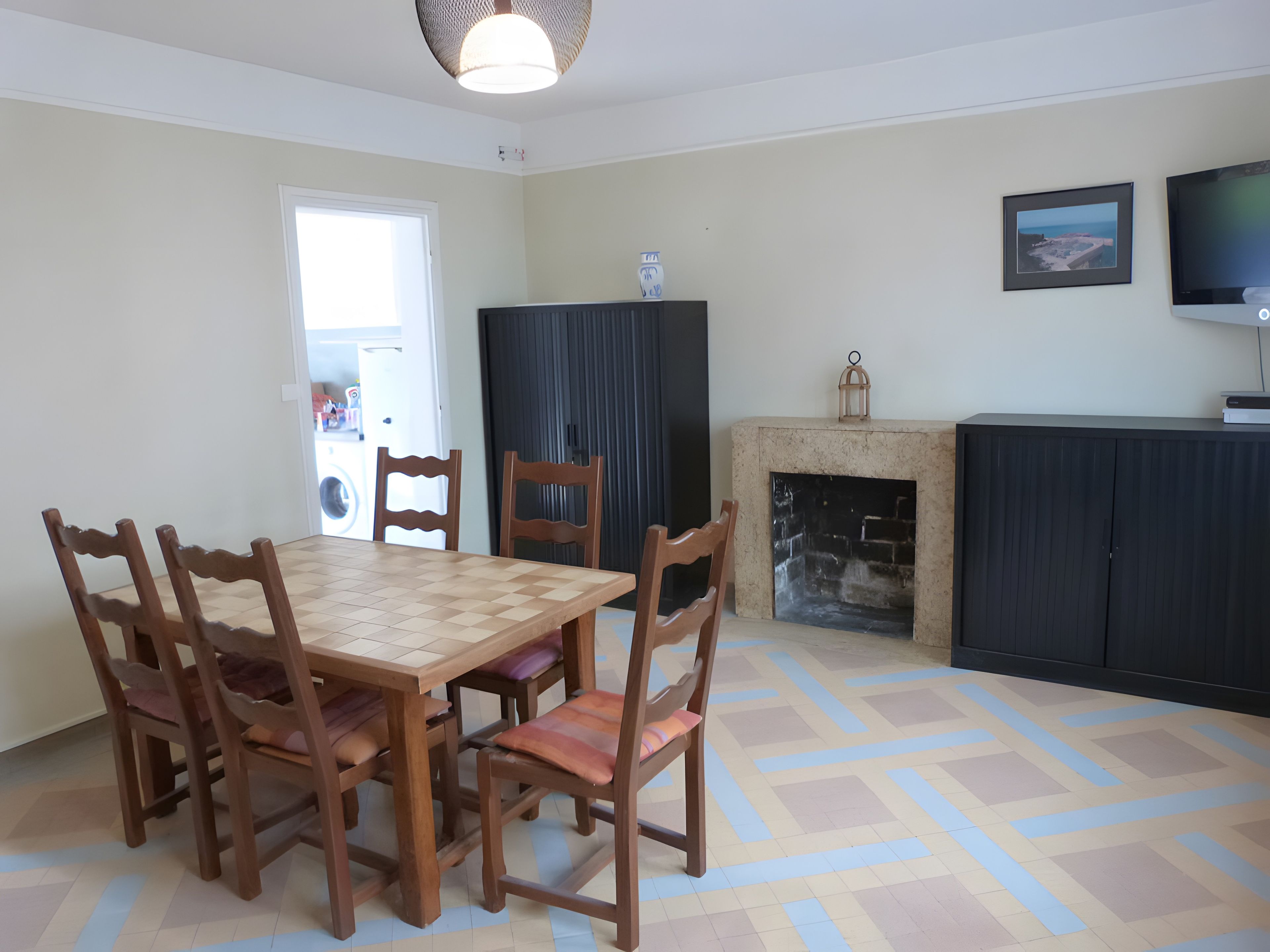 Un coin repas avec une table et des chaises en bois, une cheminée, un téléviseur et un tableau encadré au mur.