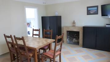 Un coin repas avec une table et des chaises en bois, une cheminée, un téléviseur et un tableau encadré au mur.