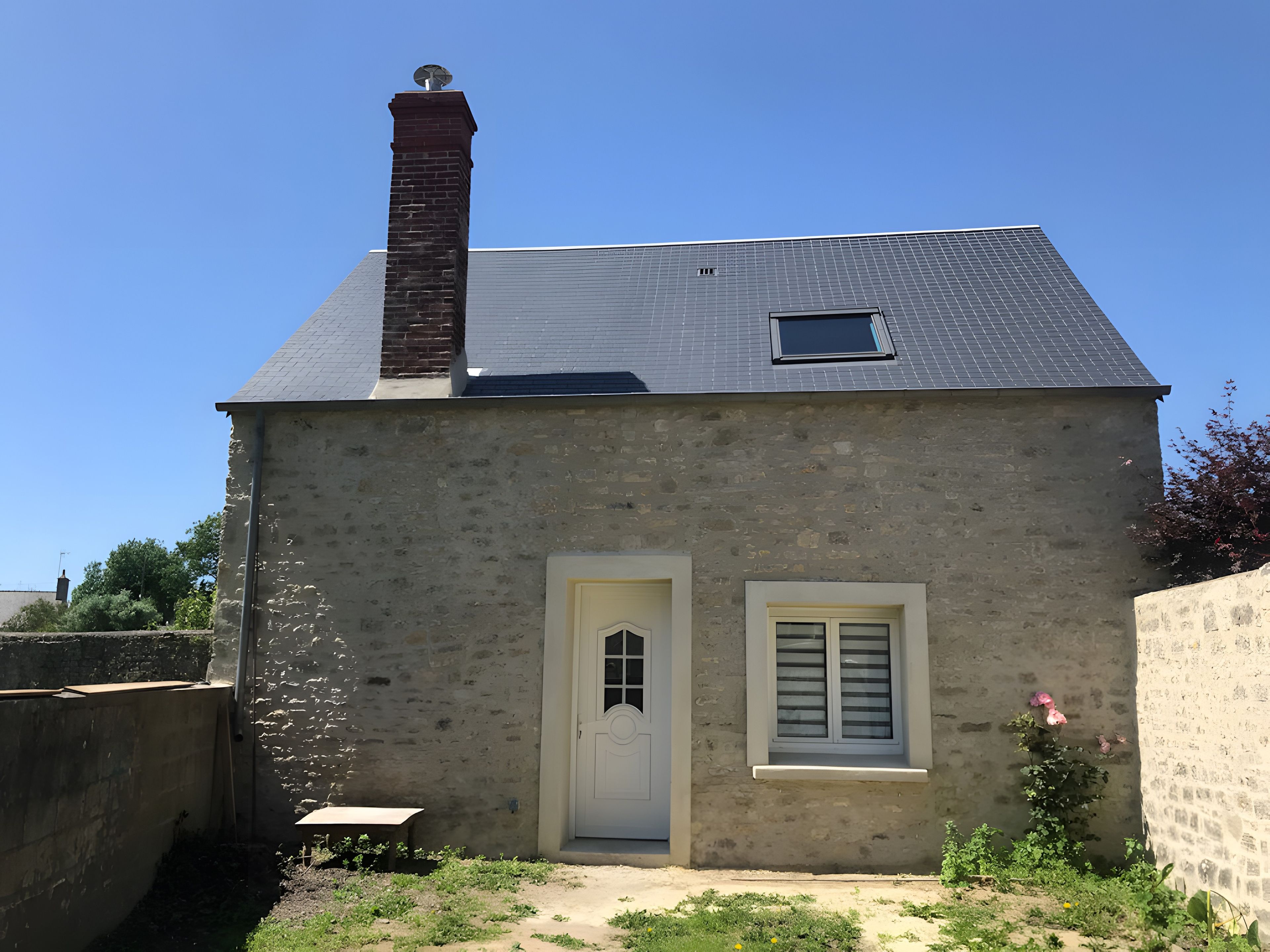 Un bâtiment à deux étages, doté d’une cheminée en briques, d’une petite fenêtre et d’une porte blanche.