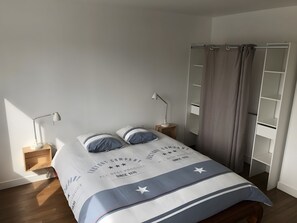 Un lit bien fait, recouvert d’une couvre-lit blanche et bleue, avec deux lampes de chevet, une table de chevet en bois et une armoire dotée d’un miroir.