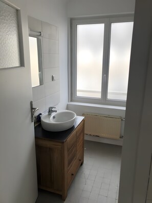 Une salle de bain avec un lavabo blanc, un meuble-lavabo en bois, un miroir et une fenêtre à vitre dépolie.
