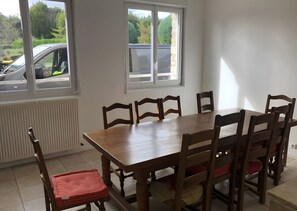 Un espace repas avec une table et des chaises en bois, de grandes fenêtres et une vue sur l’extérieur.