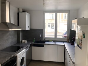 Une cuisine compacte équipée d’un lave-linge, d’un évier et d’une fenêtre donnant sur la rue.