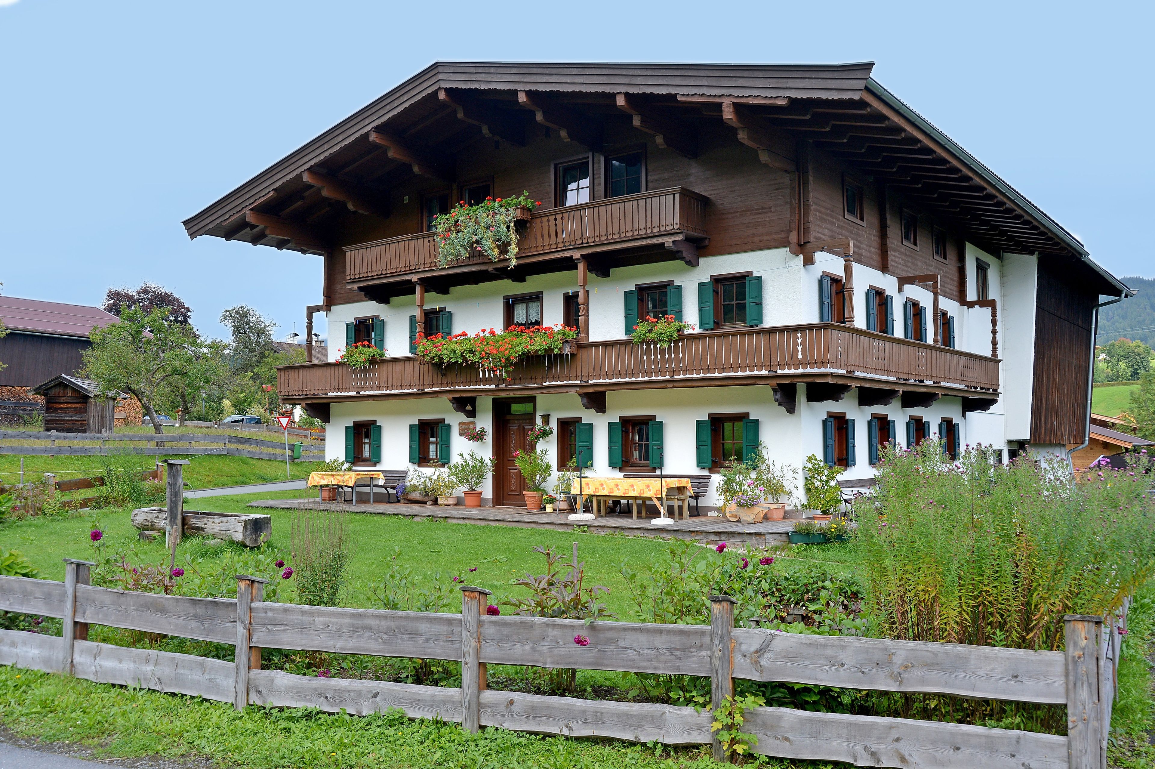 A traditional multi-story building with balconies, a wooden fence in the foreground, and a well-maintained garden.