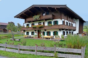 A traditional multi-story building with balconies, a wooden fence in the foreground, and a well-maintained garden.