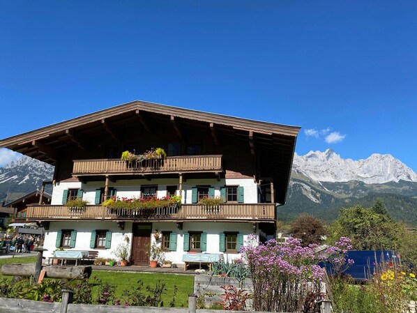 A traditional chalet with a wooden facade, balconies with flower boxes, and a mountain backdrop.