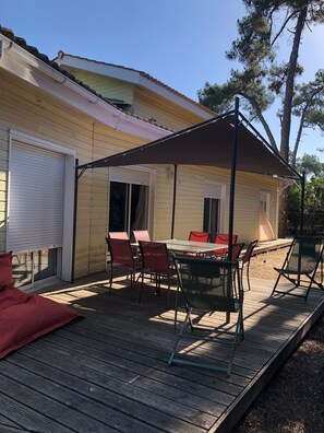 Une terrasse extérieure couverte, avec une table et des chaises, une terrasse en bois et une maison en arrière-plan.