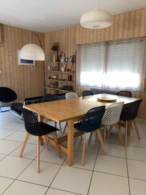 Un coin repas avec une table et des chaises en bois, une bibliothèque et une fenêtre avec des stores.