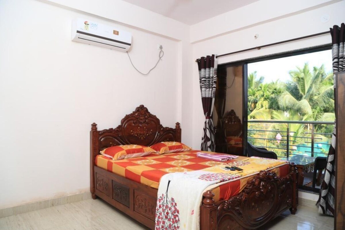A bedroom with a wooden bed, an air conditioning unit, a balcony with a view of palm trees.