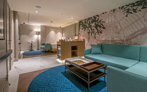 A modern living room with a teal sofa, a coffee table, a small kitchenette, and a large wall mural. - Room-luxurious Executive Family Suite in (Istanbul)