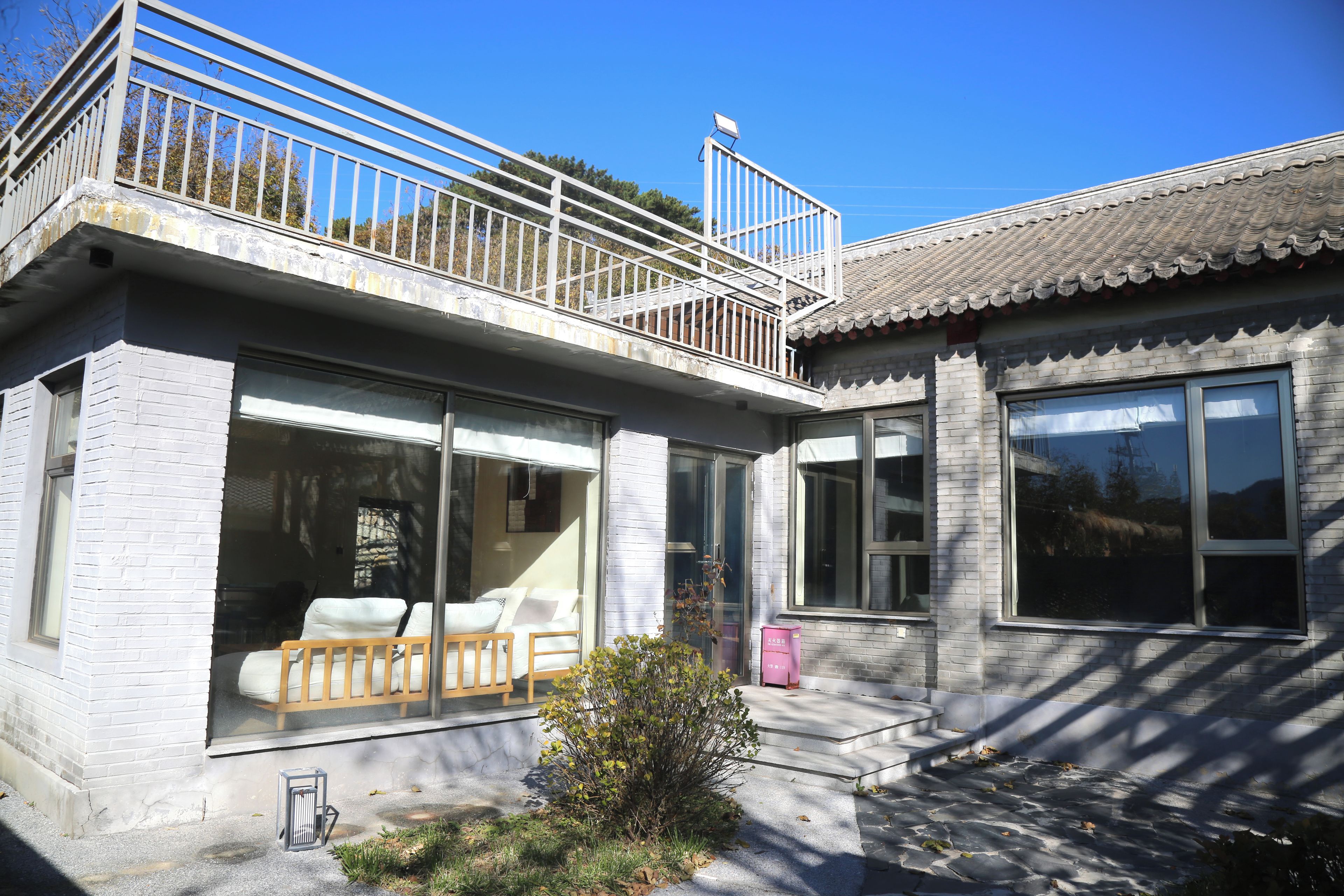 A two-story house with a balcony, large windows, and a small garden area.