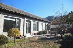 En traditionell byggnad med ett tak täckt av tegelpannor, stora fönster och en liten trädgård med ett träd och utemöbler.