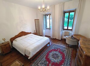 Ein Schlafzimmer mit einem Bett, einem Sessel, einem Schminktisch, einer Chandelier und einem Fenster mit Vorhängen.