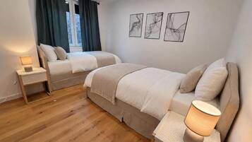 Un dormitorio con dos camas, una mesita de noche con lámpara, una ventana con cortinas y tres obras de arte en la pared.