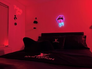 Une chambre dotée d’un lit agrémenté de linge de maison Louis Vuitton, d’un néon mural et d’un motif graphique représentant une bouche au néon.