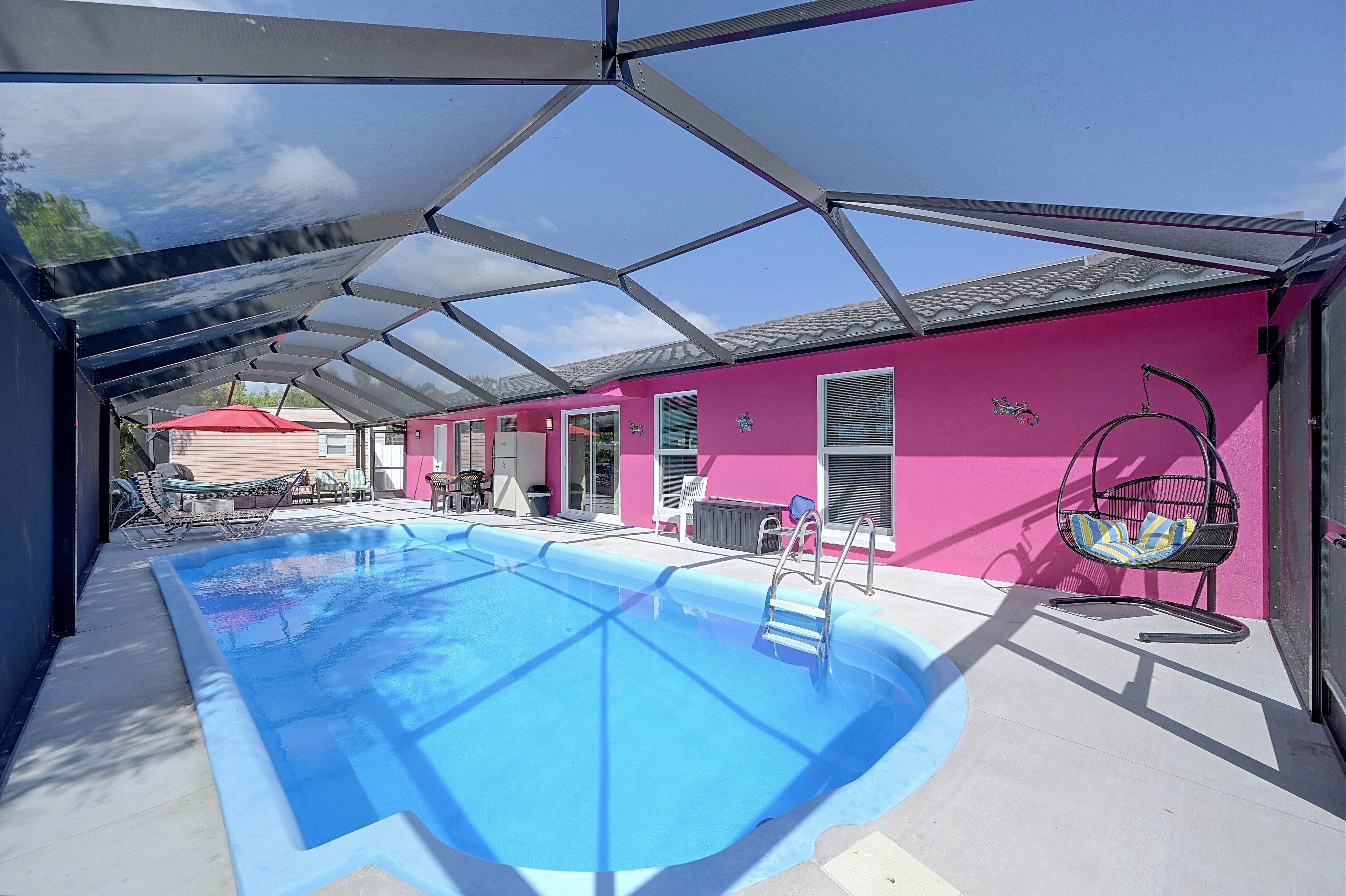 Una piscina con techo de vidrio, paredes rosas y una silla con cojín a rayas.