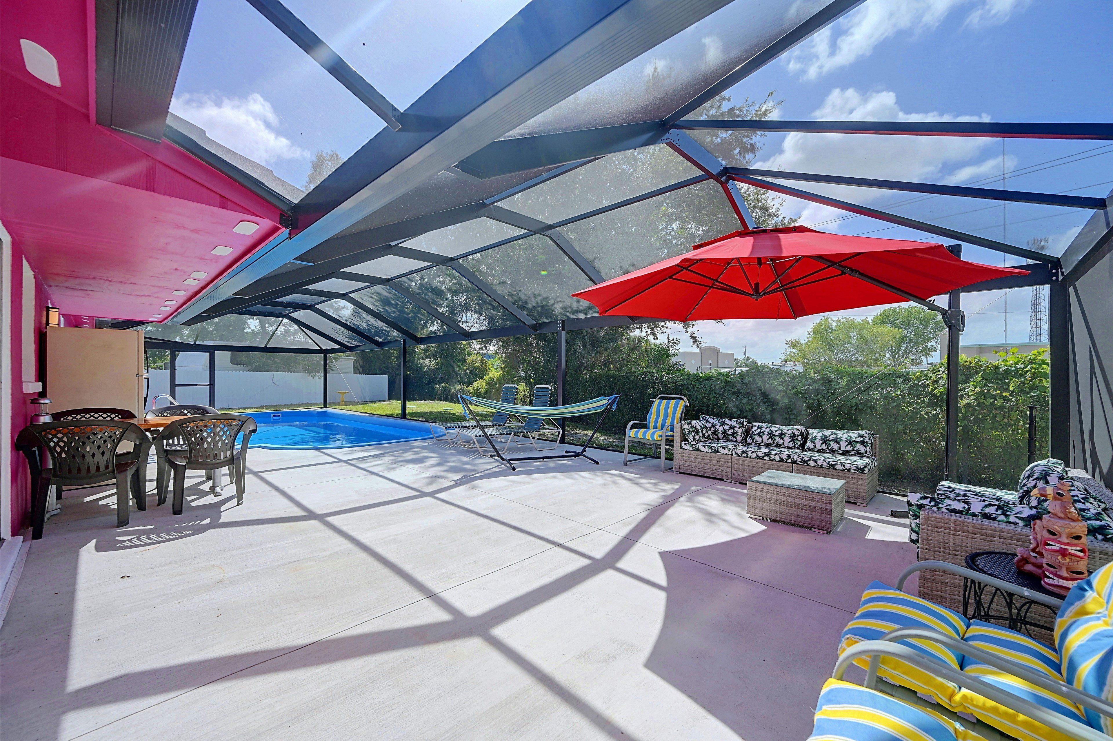Un espacio al aire libre cubierto con piscina, asientos y un paraguas rojo.