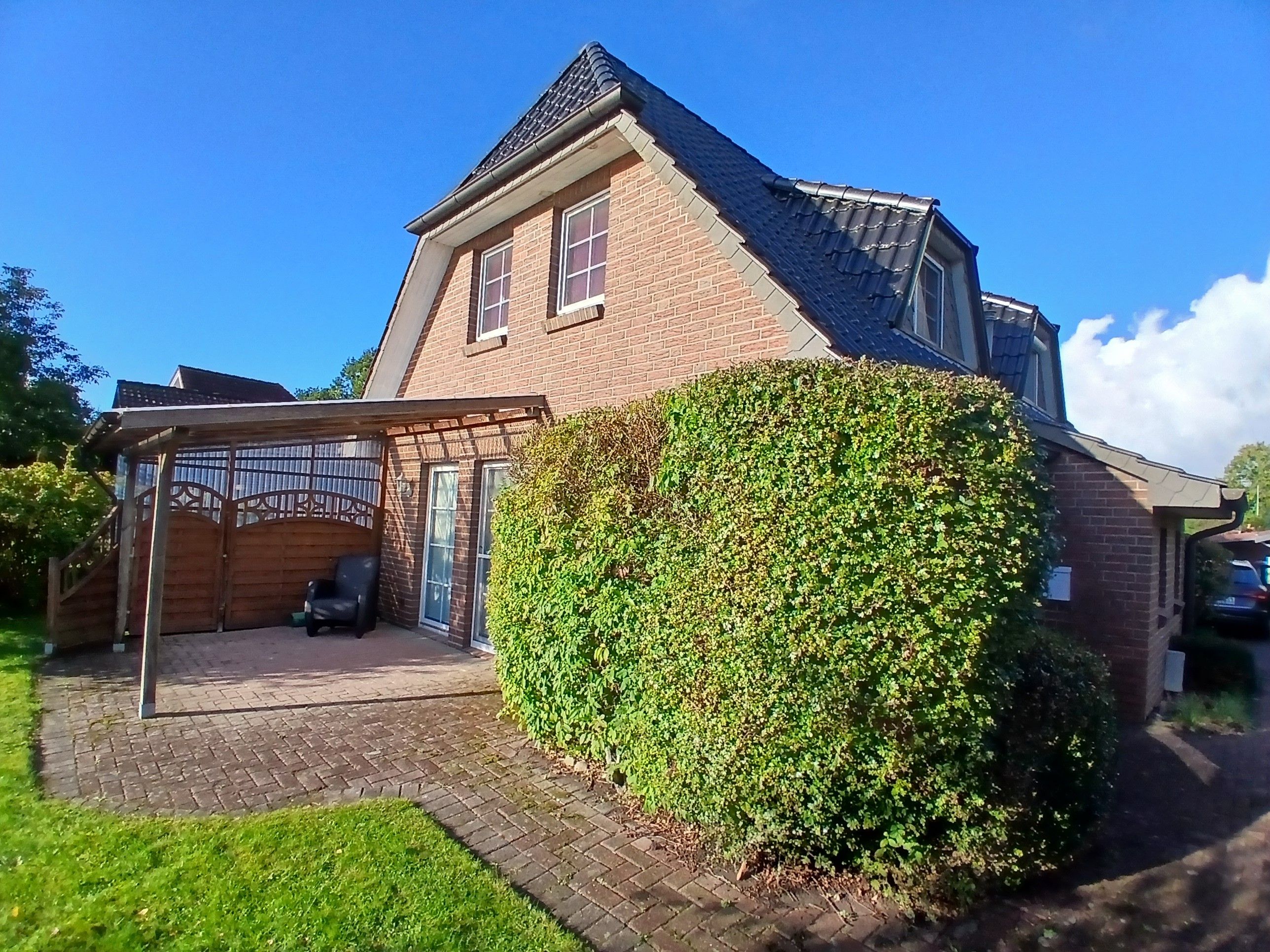 A two-story house with a brick exterior, a covered patio area, and a well-maintained hedge.