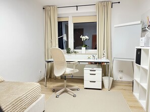Ein modernes Schlafzimmer mit einem Bett, einem Schreibtisch mit Stuhl, einer Kommode und einem Fenster mit Vorhängen.
